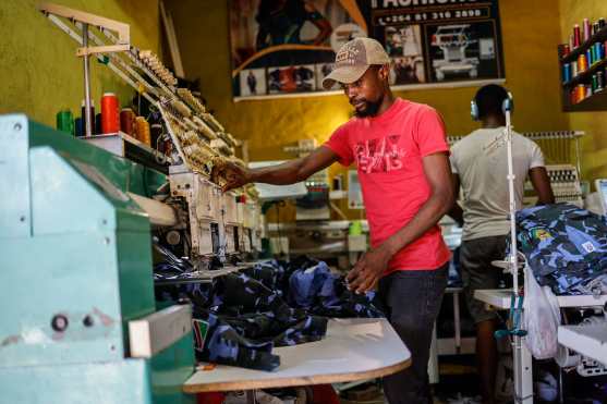 Designer and tailor Dennis Shidute (L) makes final touches on a shirt at his shop inside a wholesale market in Windhoek on November 25, 2024. (Photo by SIMON MAINA / AFP)