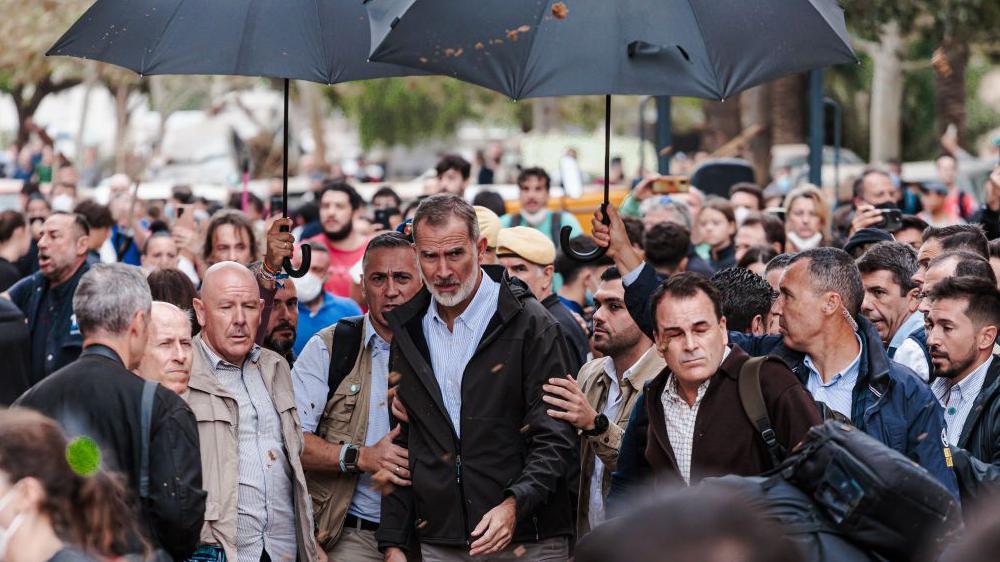 El rey tuvo que ser protegido con un paraguas del lanzamiento de barro y otros objetos. 