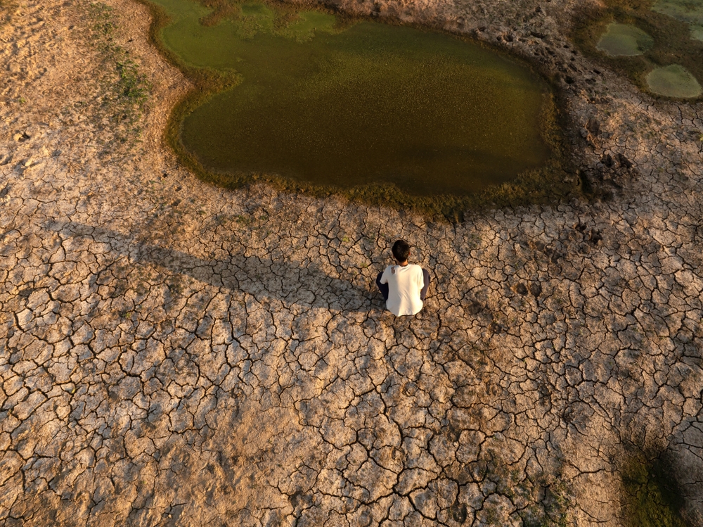 Hombre sentado cerca de la sequía de la metáfora del río, la crisis del agua, la sequía y el cambio climático