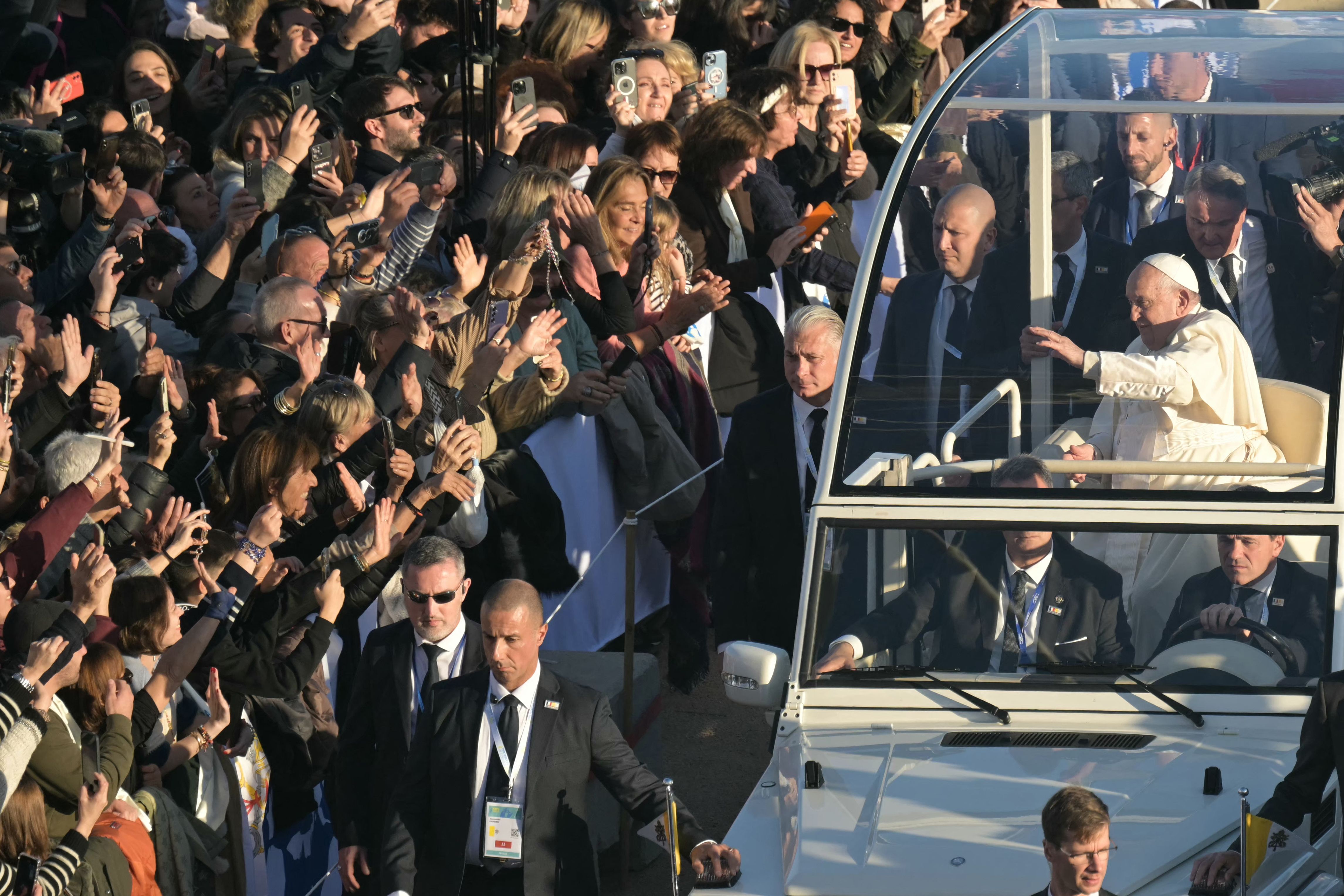 Pope Francis (C) greets the crowd as he rides the popemobile car at Place Miot in Ajaccio, as part of his trip on the French island of Corsica, on December 15, 2024. Pope Francis visits Corsica, a stronghold of the Catholic faith with locals hotly anticipating the first-ever trip by a pontiff to the French Mediterranean island. His short trip, based around a congress on faith in the Mediterranean region, comes just a week after he snubbed the re-opening of Notre Dame cathedral in Paris five years after a devastating fire. (Photo by Bertrand GUAY / AFP)