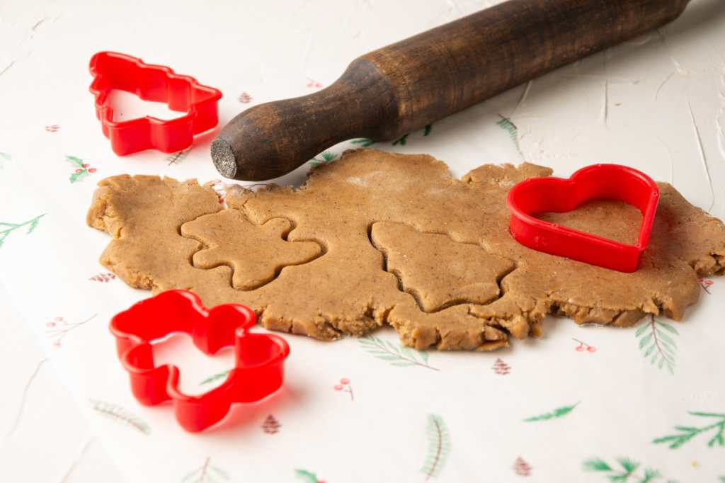 Vista superior de la masa de galletas de jengibre con moldes de Navidad rojos sobre papel blanco con rodillo, horizontal