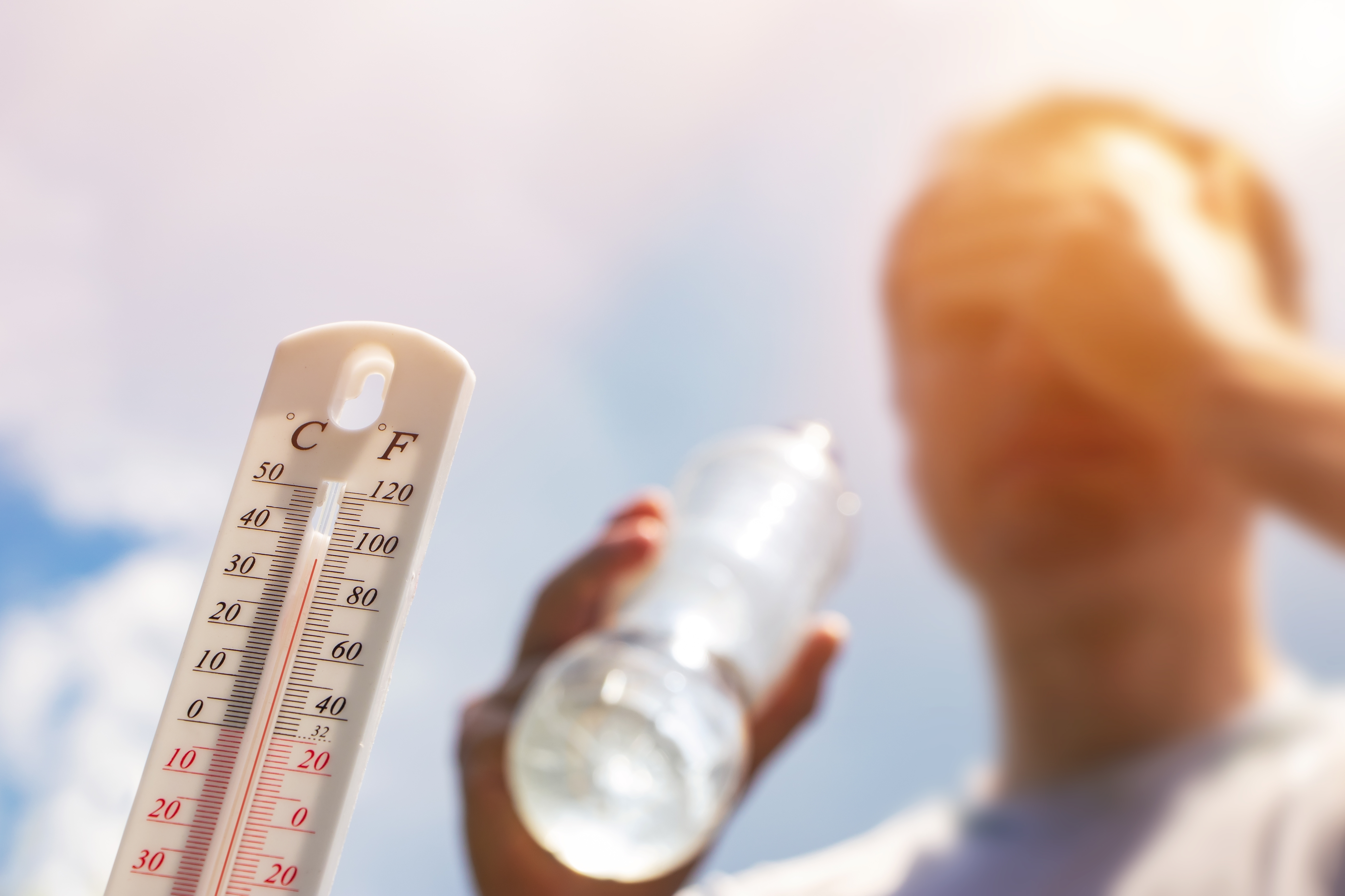 El hombre bebe agua en calor extremo, el termómetro en el día de verano muestra o indica un alto grado de temperatura con el sol en el fondo.