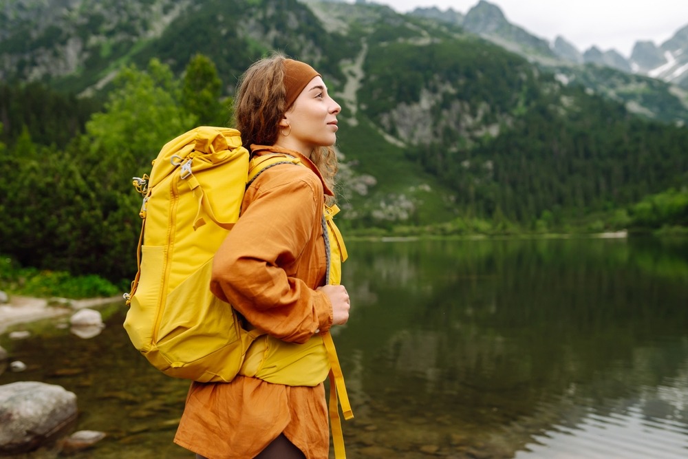 Mujer feliz con una mochila de senderismo amarilla disfrutando del paisaje de montaña. Aventura, viaje, deporte, vida activa.