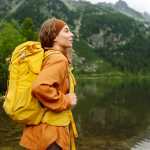 Mujer feliz con una mochila de senderismo amarilla disfrutando del paisaje de montaña. Aventura, viaje, deporte, vida activa.