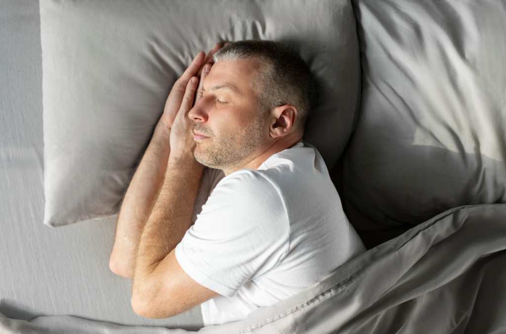 Hombre de mediana edad europeo tranquilo que duerme de lado en la cama en casa, disfrutando de su almohada y colchón cómodos, vista superior sobre la cama. Saludable, buen sueño