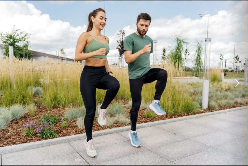 Pareja energética en ropa deportiva realiza ejercicios dinámicos de rodilla alta en un espacio verde urbano.