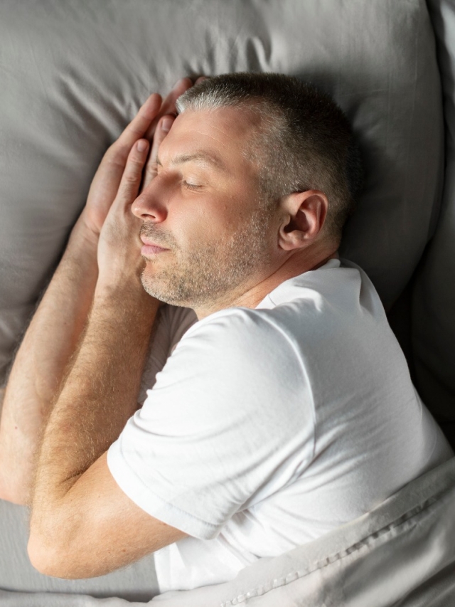 Hombre de mediana edad europeo tranquilo que duerme de lado en la cama en casa, disfrutando de su almohada y colchón cómodos, vista superior sobre la cama. Saludable, buen sueño