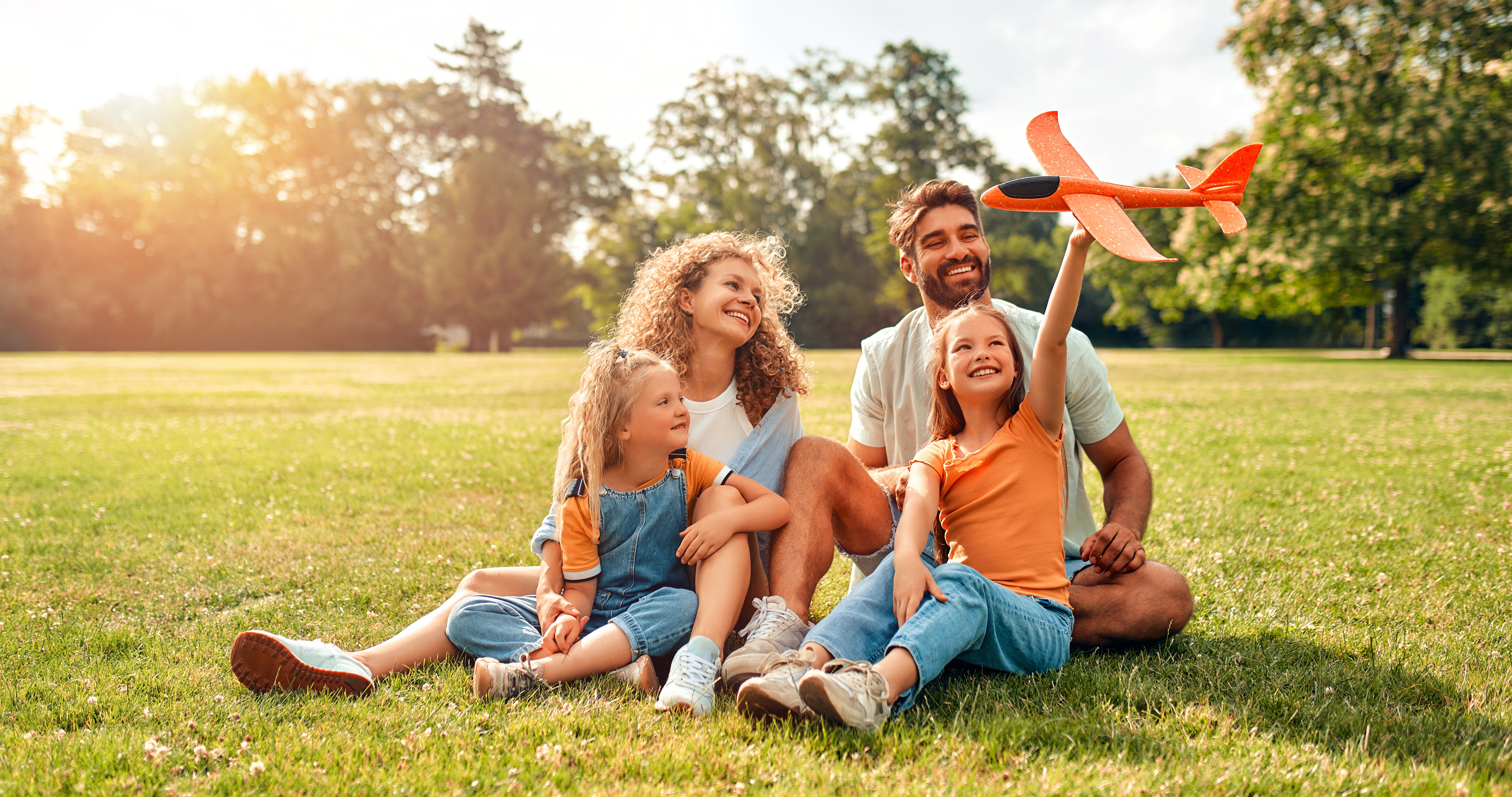 Feliz padre de familia, madre y dos hijas niños jugando con un avión sentado en un prado en el pasto en el parque en un cálido día soleado, divirtiéndose en un día libre.