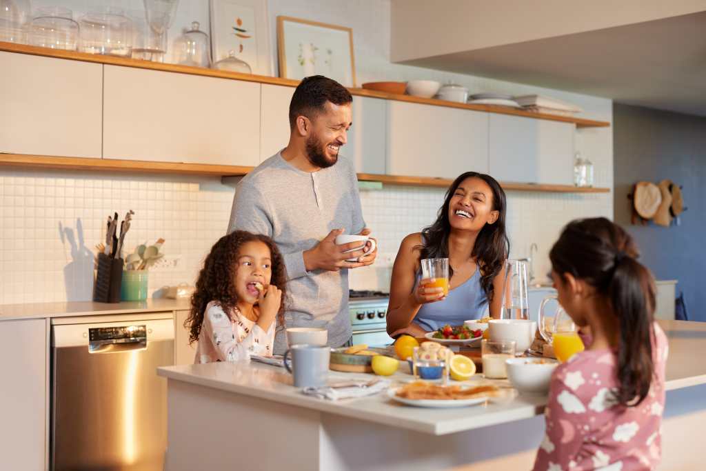 Familia hispana disfruta de un alegre desayuno juntos en la cocina moderna. Familia de raza mixta con dos hijas compartiendo una alegre comida matutina alrededor de la isla de la cocina. Familia multiétnica desayunando