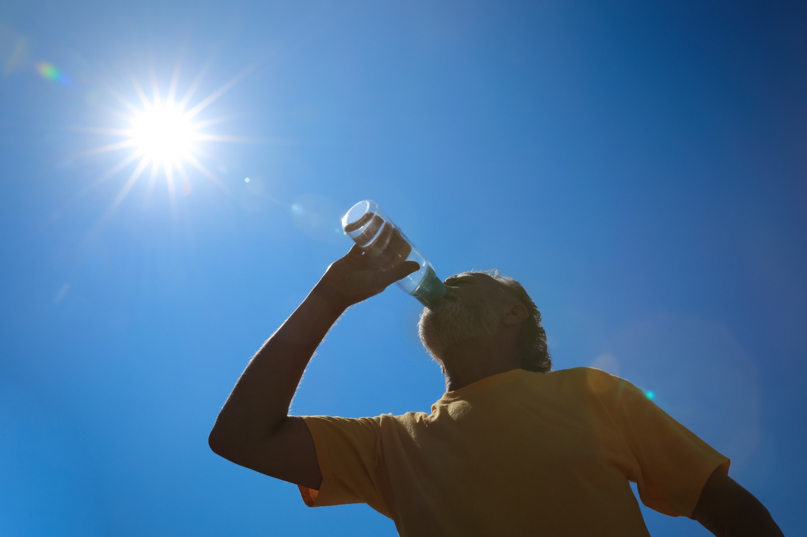 Hombre mayor bebiendo agua para evitar golpes de calor al aire libre, vista de ángulo bajo