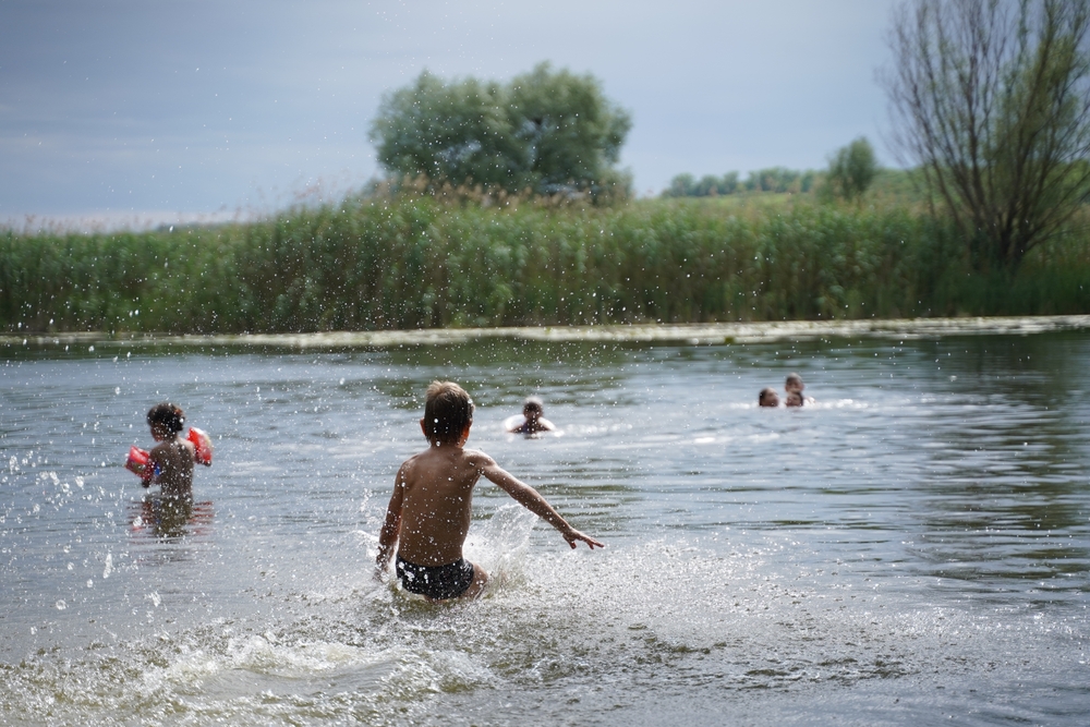 Un chico feliz corre de la orilla al agua. Vacaciones infantiles de verano a orillas del lago o del río. los niños saltan al agua, nadan y se bañan al atardecer. Vacaciones activas. Enfoque selectivo