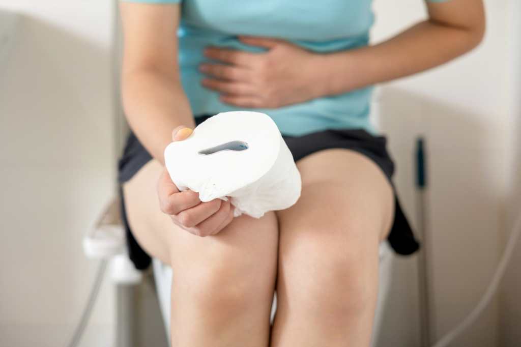 Mujer estreñida que sufre de dolor mientras está sentada en el inodoro y sostiene el papel higiénico