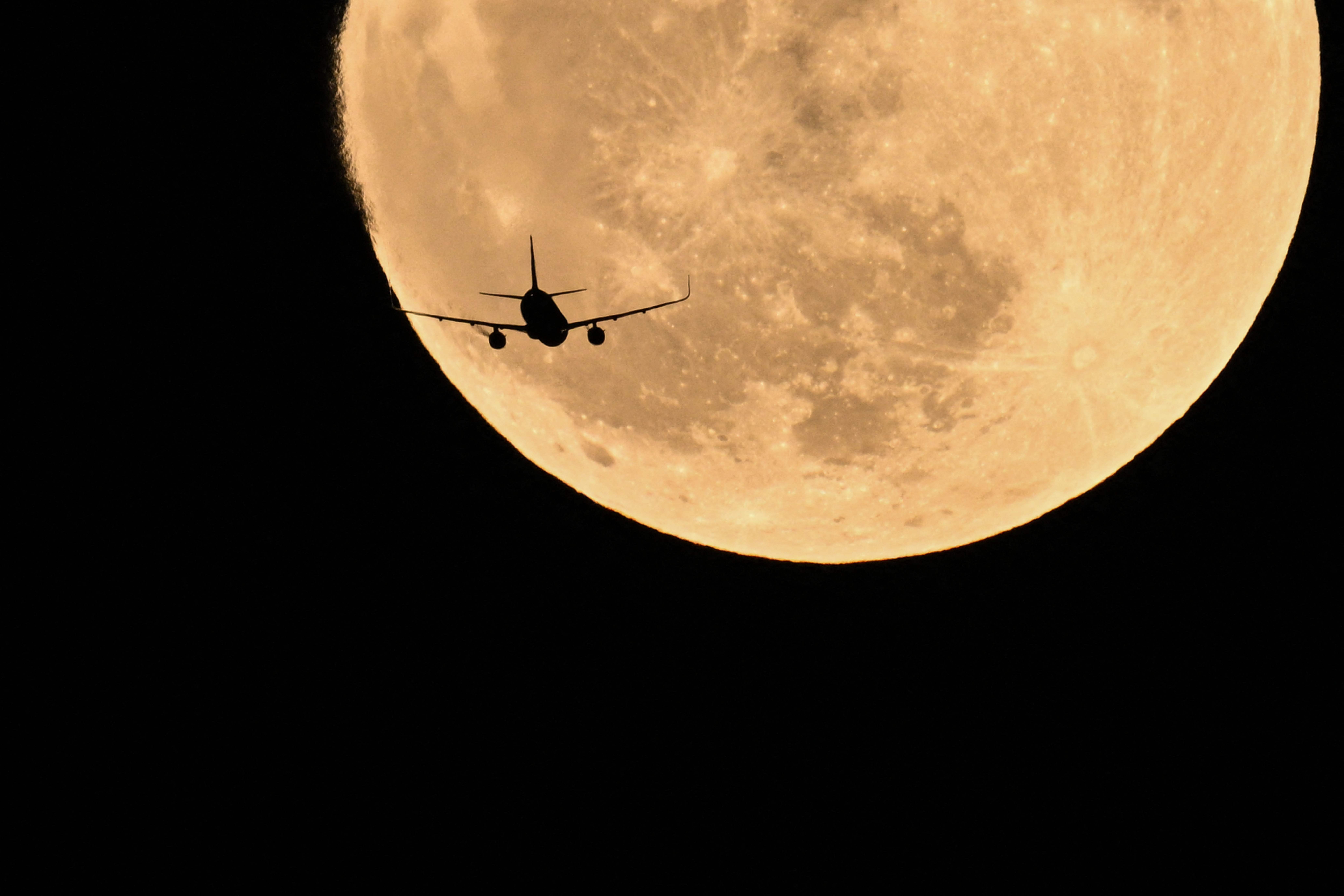 Un avión pasa frente a la luna llena, conocida como "Luna de fresa", en China. (Foto Prensa Libre: AFP)