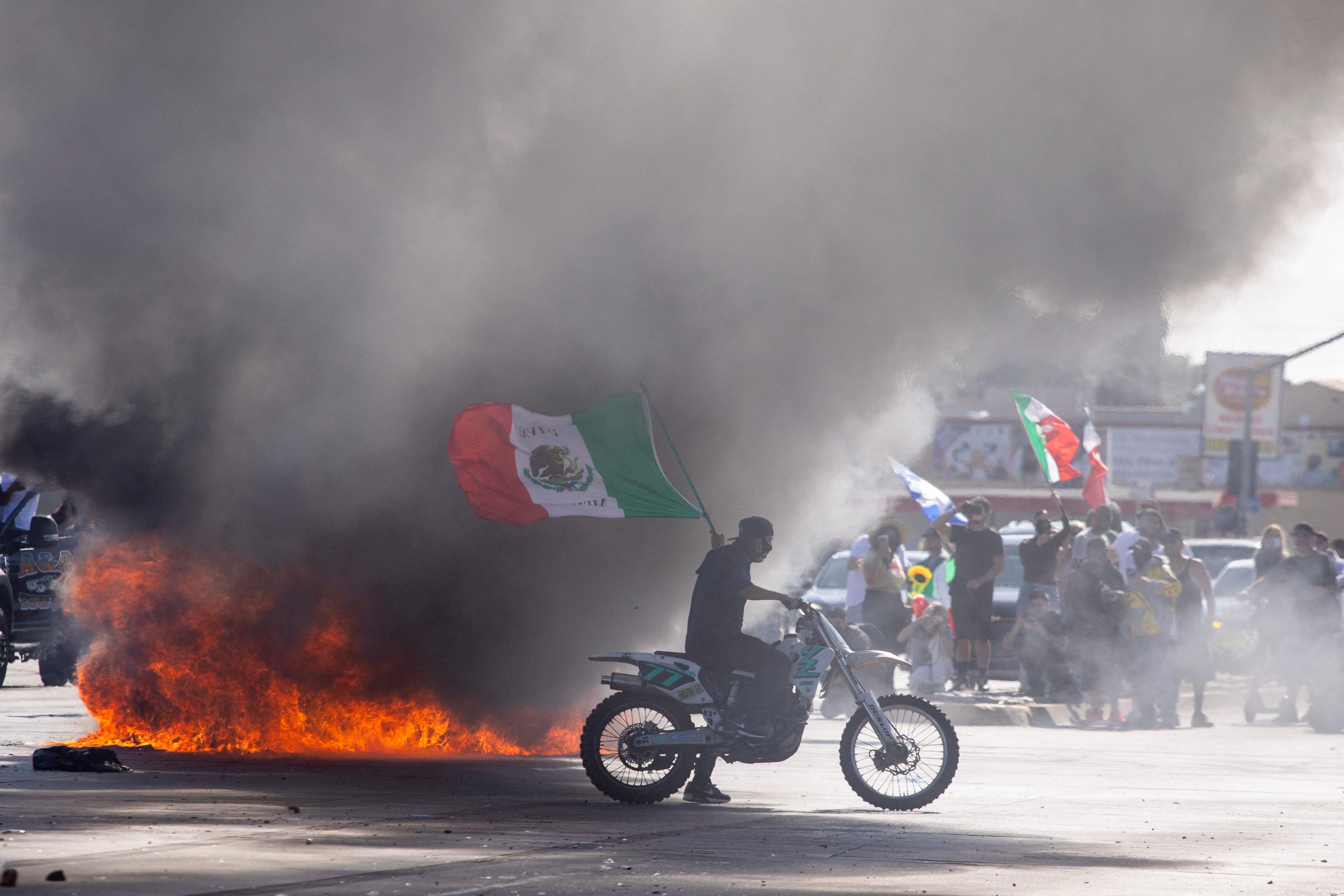 Un manifestante porta la bandera mexicana cerca de un vehículo en llamas, en Los Ángeles, California. (Foto Prensa Libre: AFP). 