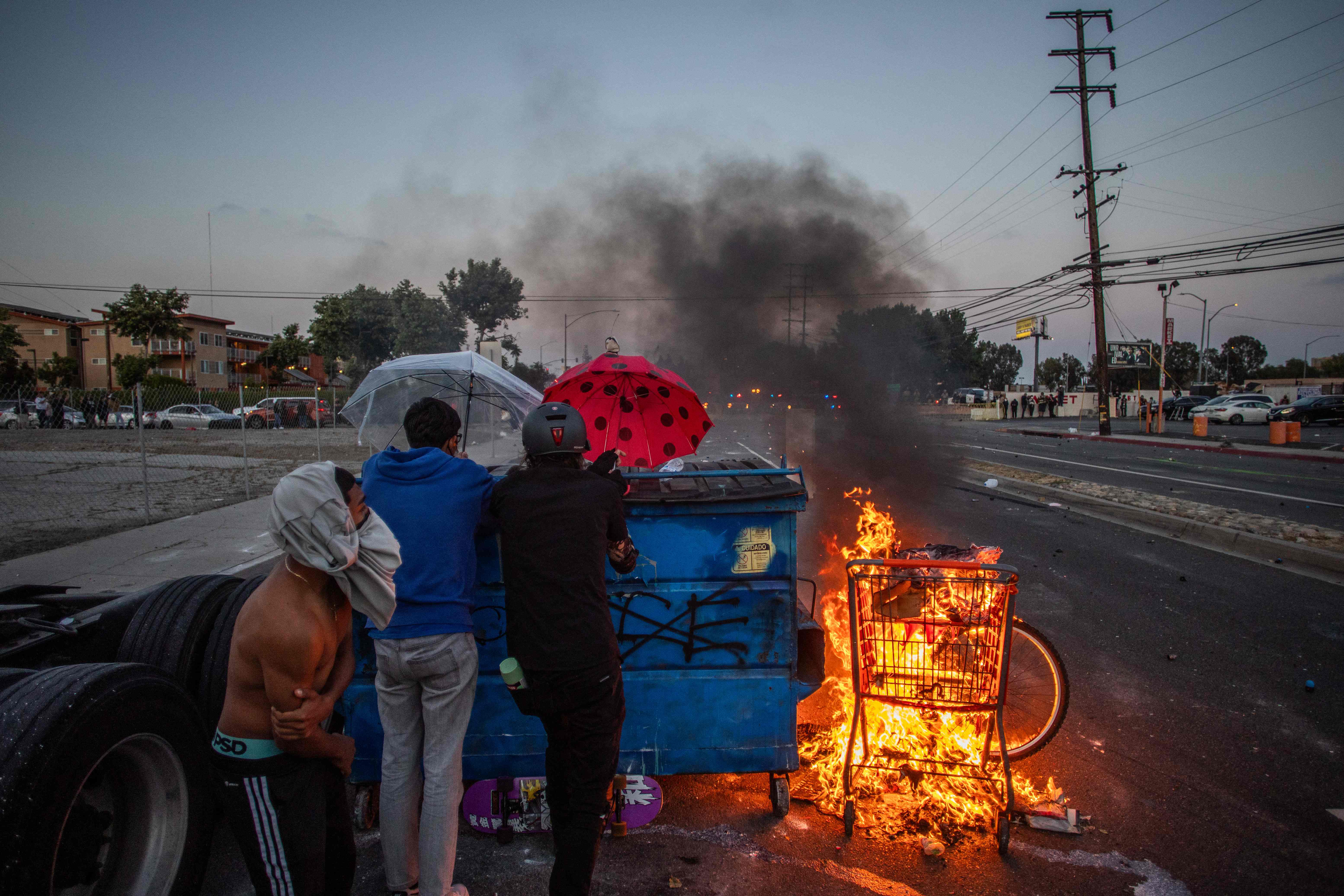 Manifestantes se cubren tras una barricada en llamas, en el tercer día de protestas contra las redadas contra migrantes indocumentados en Los Ángeles. (Foto Prensa Libre: AFP)