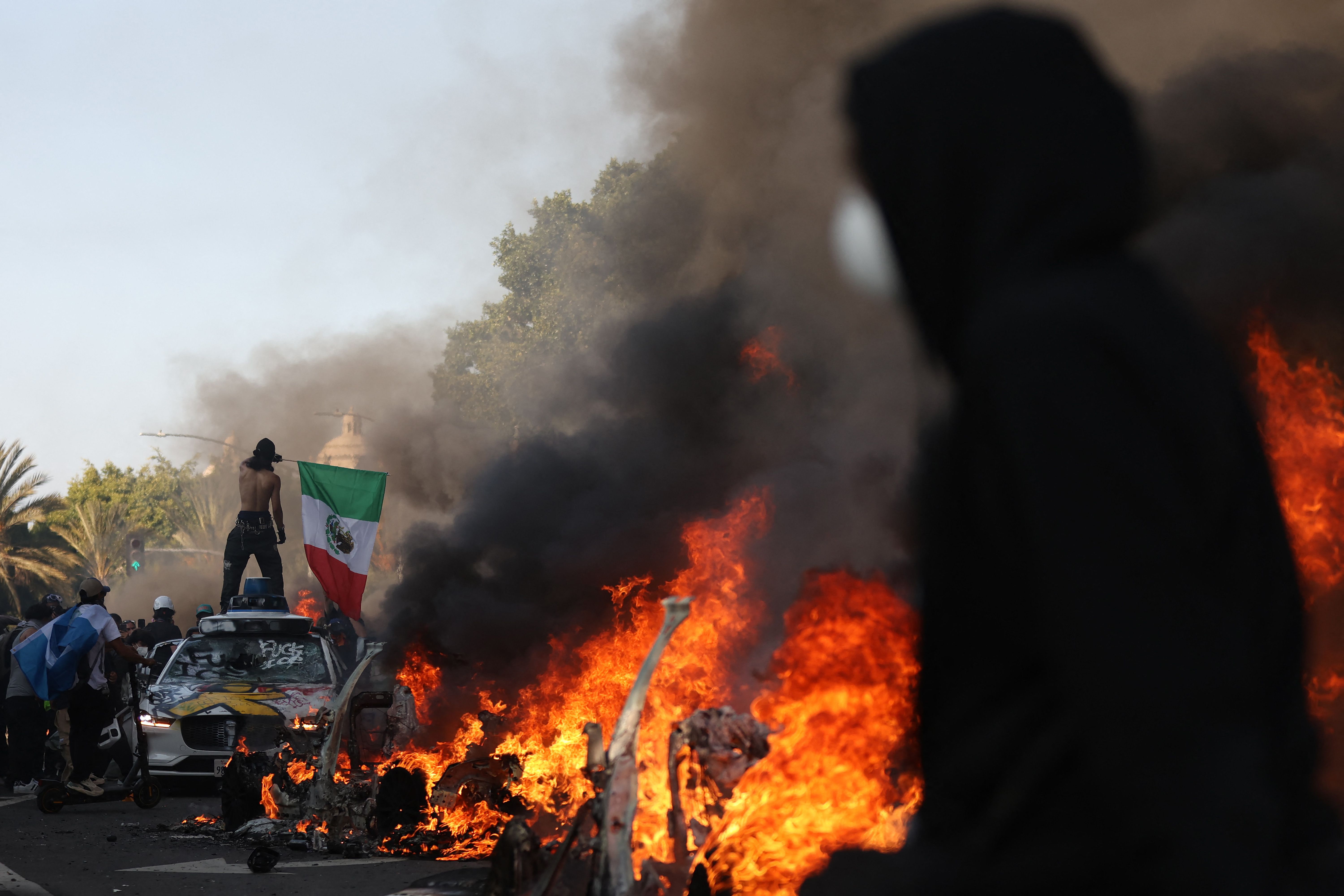 Autos en llamas bordean una calle mientras la gente protesta el 8 de junio de 2025 en Los Ángeles, California. (Foto Prensa Libre: AFP)