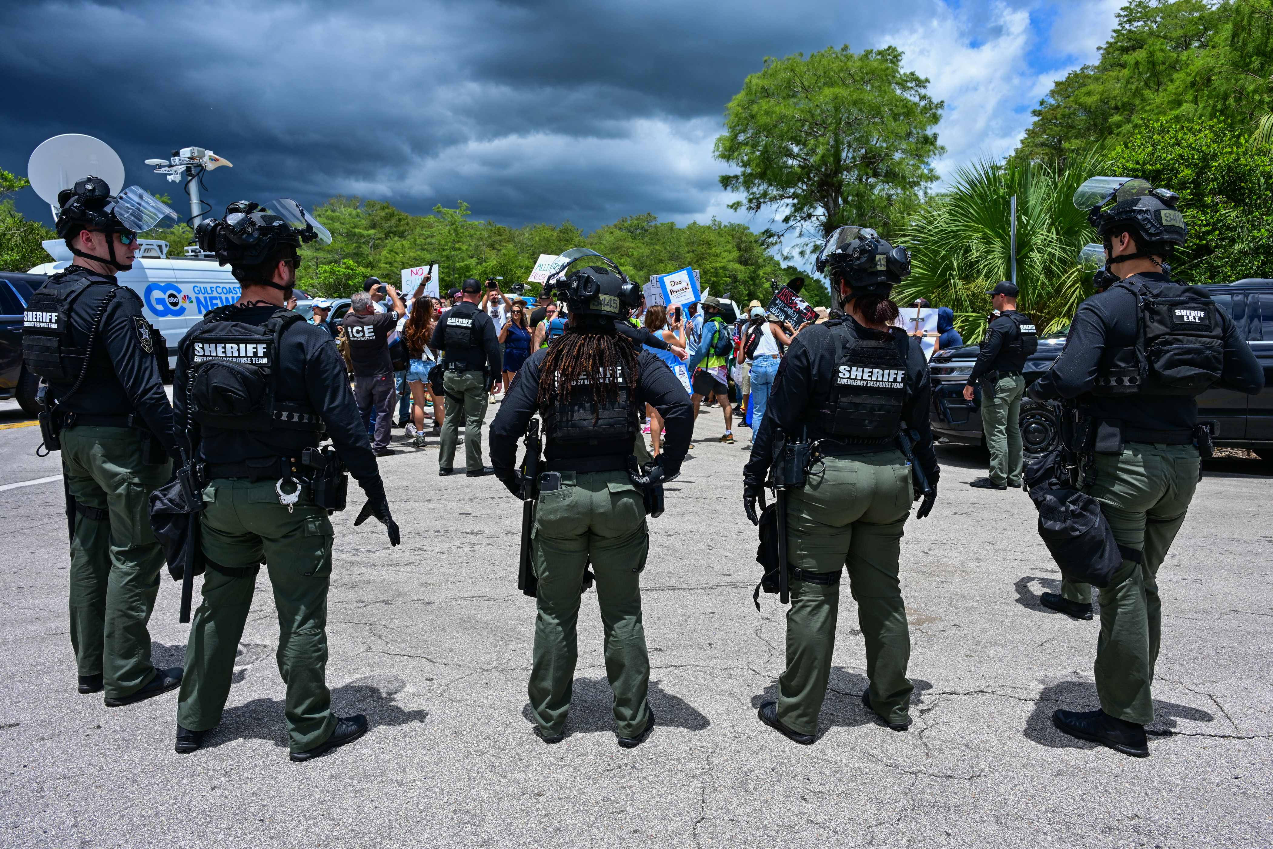 Agentes de policía resguardan mientras manifestantes protestan contra la visita del presidente estadounidense Donald Trump a un centro de detención de migrantes, conocido como "Alligator Alcatraz", ubicado en el antiguo Aeropuerto de Entrenamiento y Transición Dade-Collier en Ochopee, Florida. (Fotografía Prensa Libre: AFP)