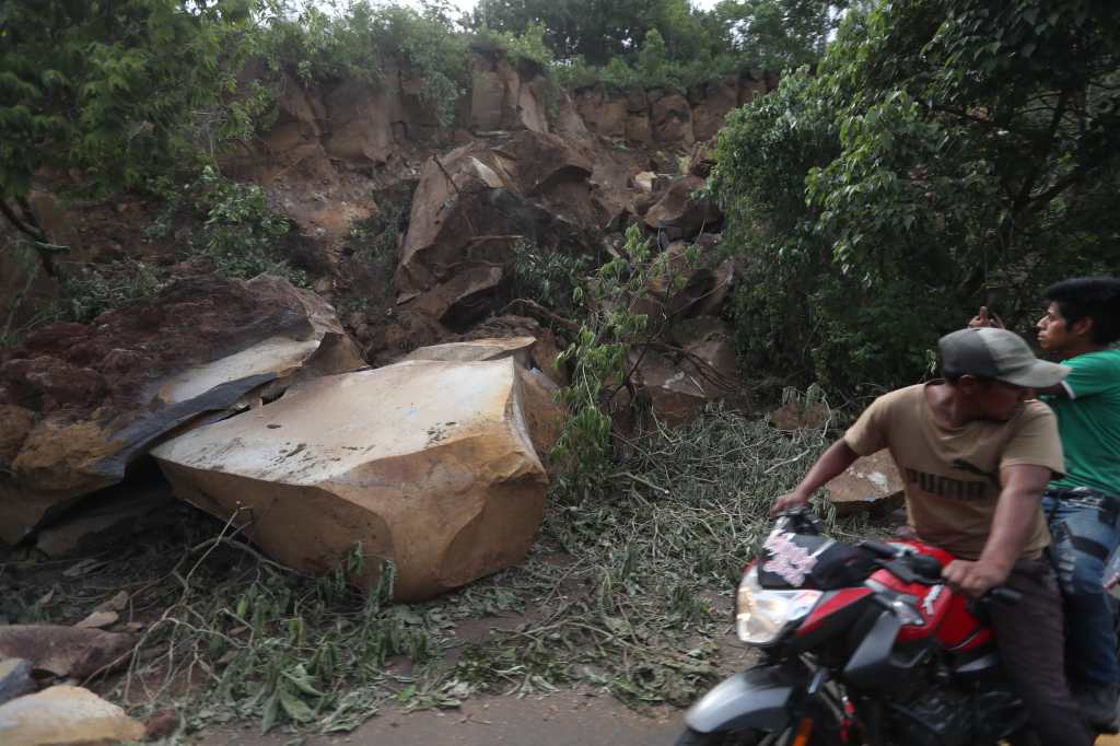 Hombre en moto pasa junto a una roca de gran tamaño que bloquea parcialmente la carretera hacia Palín.
