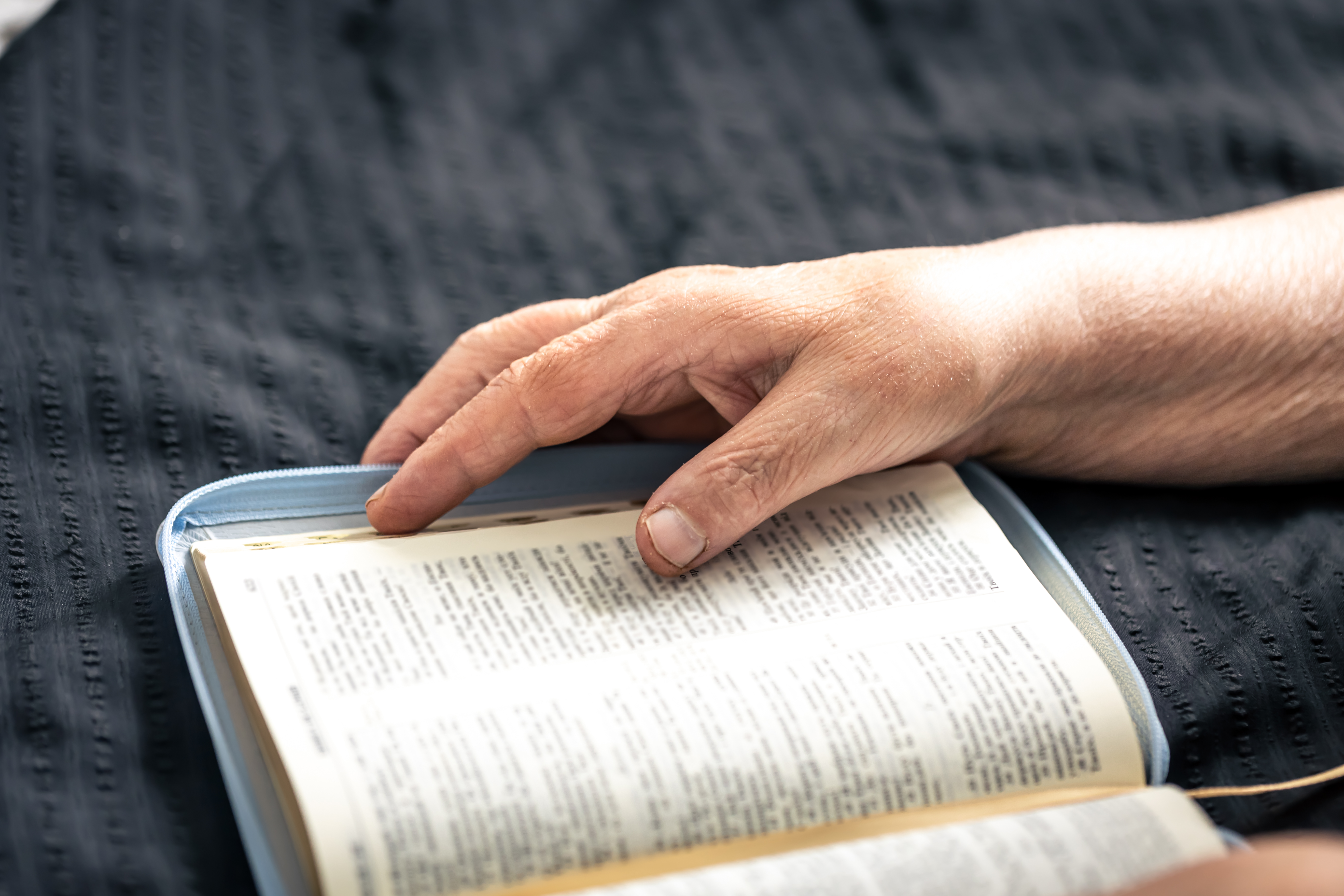 An elderly woman reads a book of the Bible, hands and close-up, the concept of faith in God and religious life.