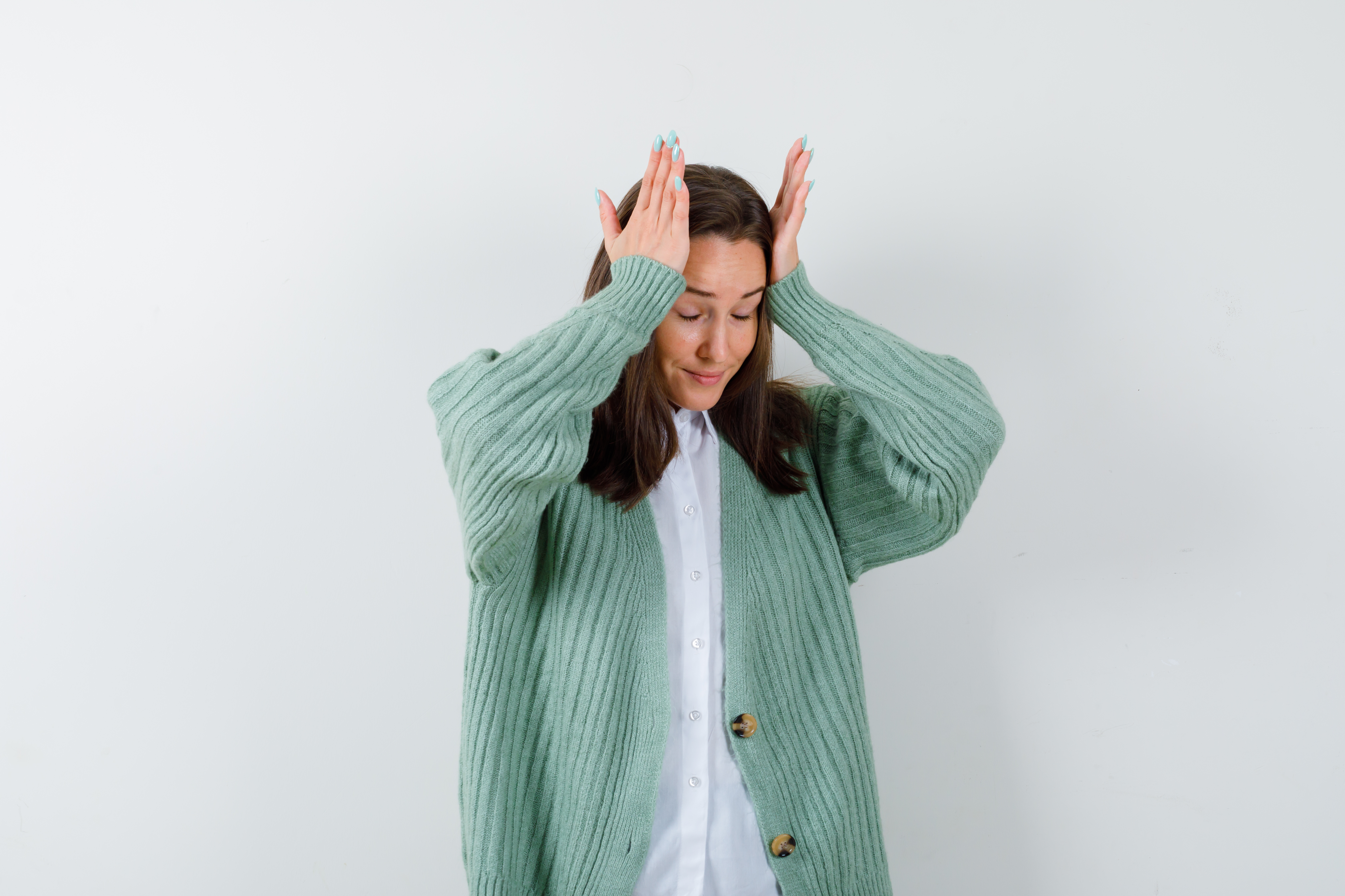 young lady keeping hands on head in blouse, cardigan and looking wistful , back view.