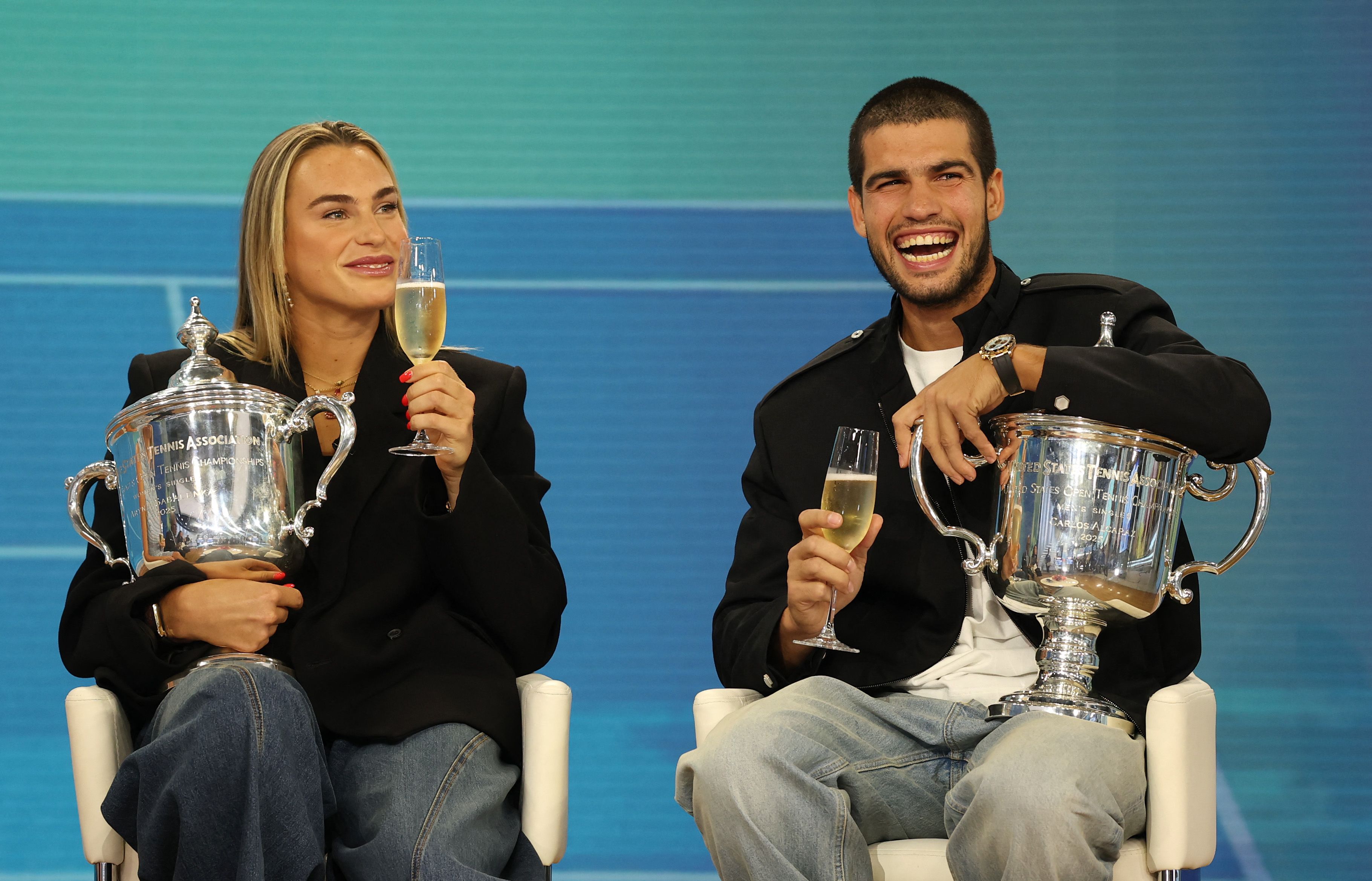 NEW YORK, NEW YORK - SEPTEMBER 08: US Open 2025 Champions Aryna Sabalenka and Carlos Alcaraz of Spain hold a glass of champagne as they are interviewed holding their trophies while filming for the Today Show following following their victories in the Men's and Women's Singles finals at Rockefeller Plaza on September 08, 2025 in New York City.   Clive Brunskill/Getty Images/AFP (Photo by CLIVE BRUNSKILL / GETTY IMAGES NORTH AMERICA / Getty Images via AFP)