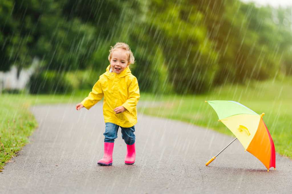 Un niño feliz y gracioso con paraguas multicolor bajo el día de lluvia de verano