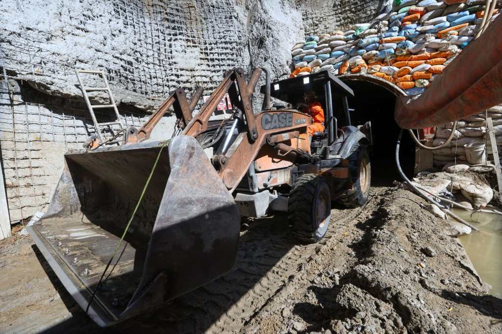 Retroexcavadora sale del acceso de la bóveda, rodeada de tierra y agua. 