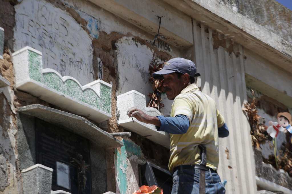 Trabajador frente a una lápida, subido en una escalera para llegar a un nicho alto.