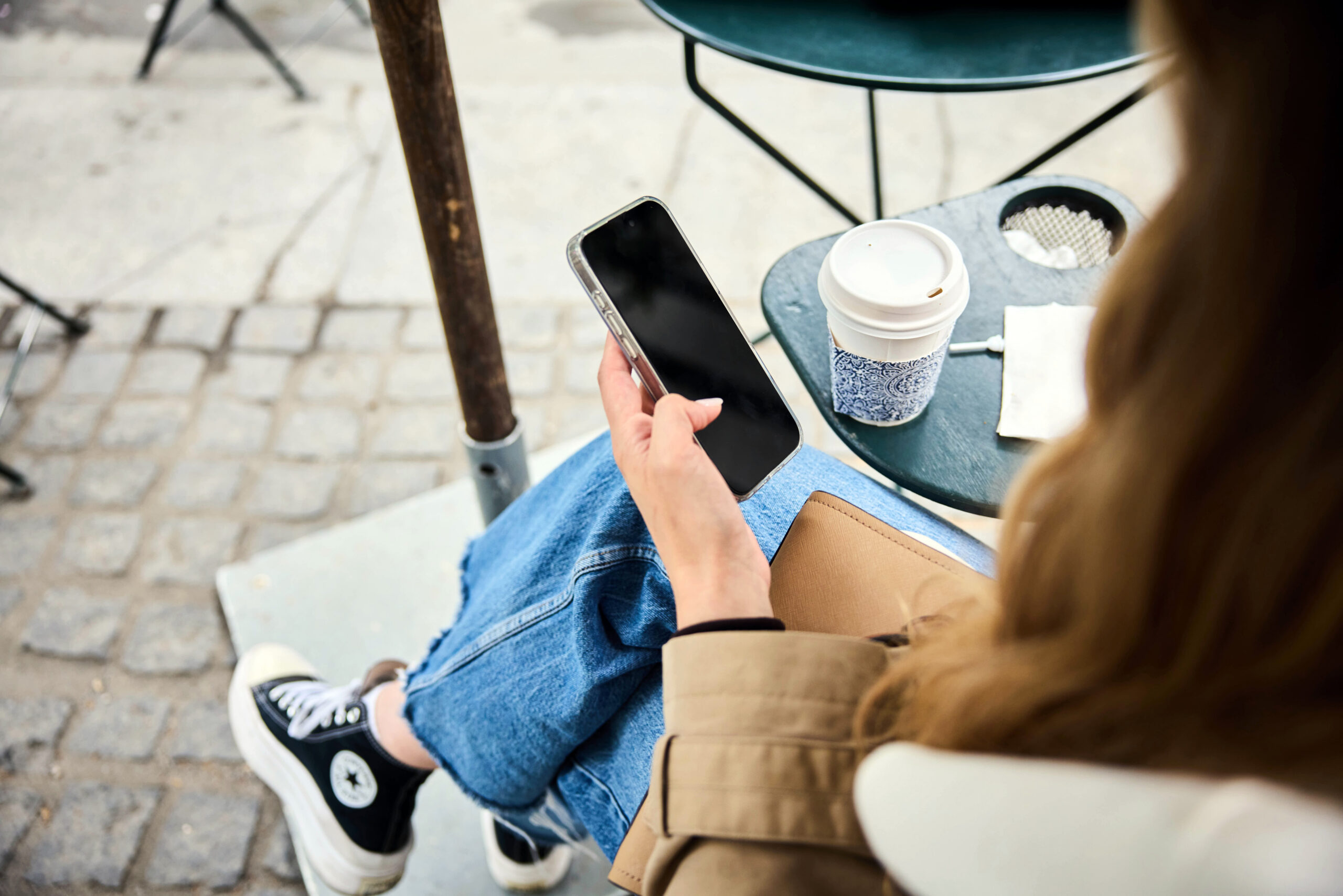 FILE -- A woman checks her smartphone at an outdoor cafe in New York, June 9, 2025. Modern smartphones rolled out in 2007, the year that fertility rates began falling. Two studies say that is not a coincidence. (Colin Clark/The New York Times)