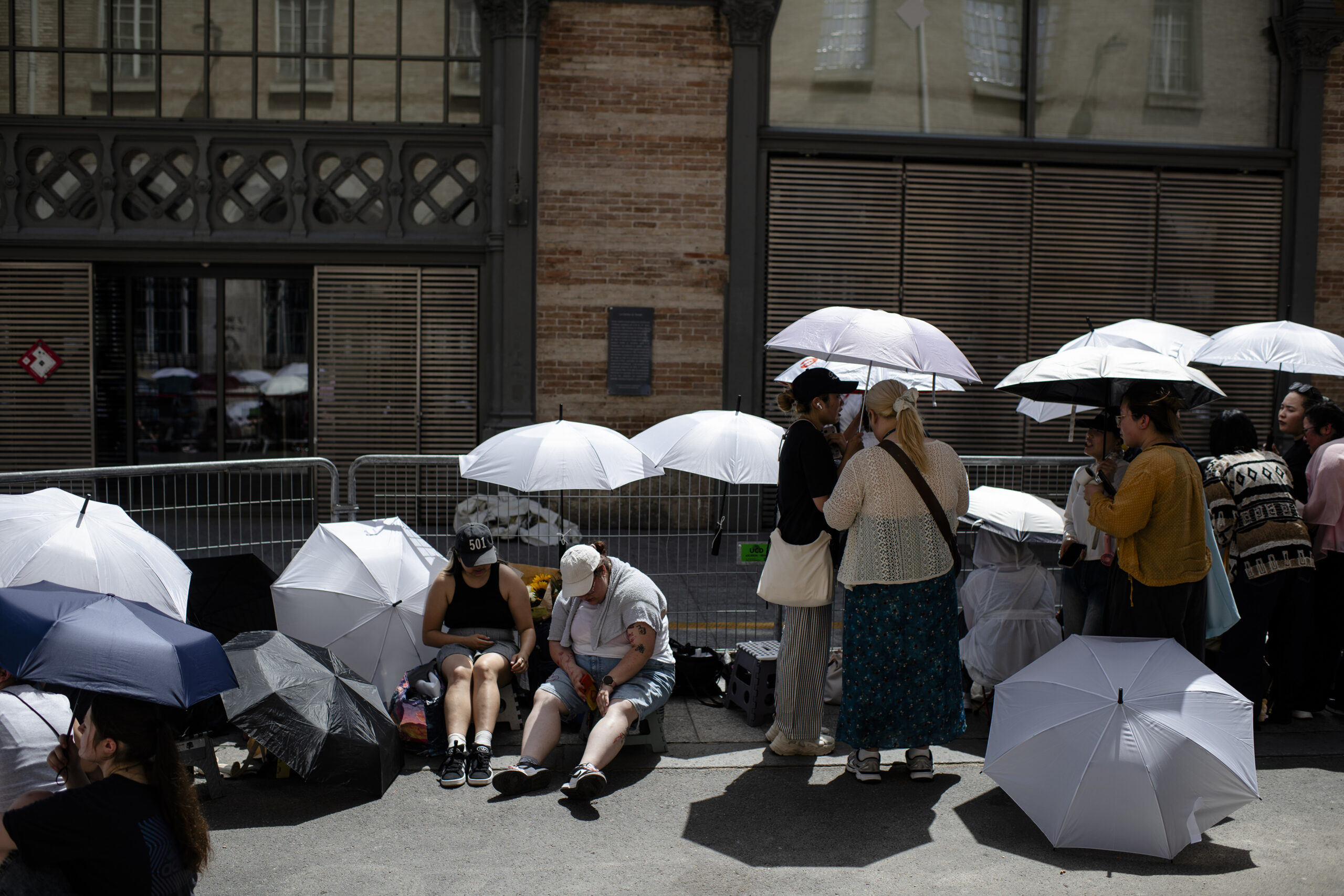FILE -- People use umbrellas for shade, as they wait for celebrities after a fashion show, during a heat wave in Paris on June 25, 2026. A growing body of research has shown that our brains work differently when temperatures spike. (Dmitry Kostyukov/The New York Times)