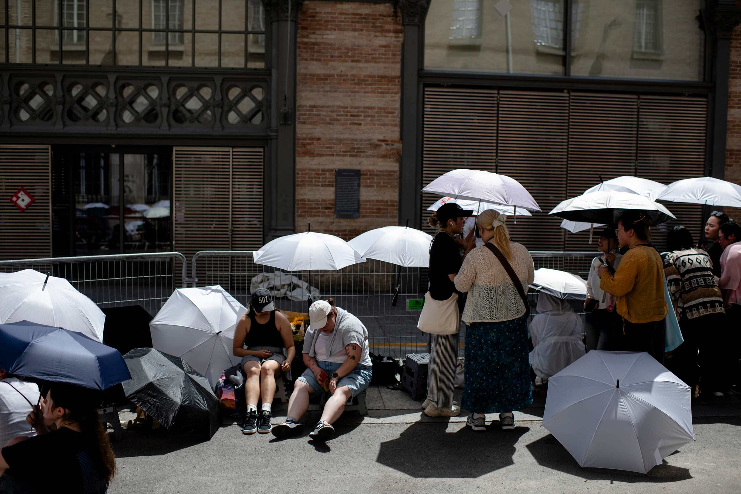 FILE -- People use umbrellas for shade, as they wait for celebrities after a fashion show, during a heat wave in Paris on June 25, 2026. A growing body of research has shown that our brains work differently when temperatures spike. (Dmitry Kostyukov/The New York Times)